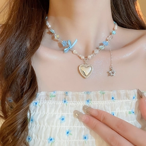 Détail d'un collier de perles argenté avec nœud bleu, pendentif cœur et breloque étoile
