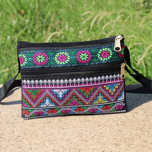 Detailed view of colorful ethnic floral embroidery on a black canvas crossbody bag outdoors