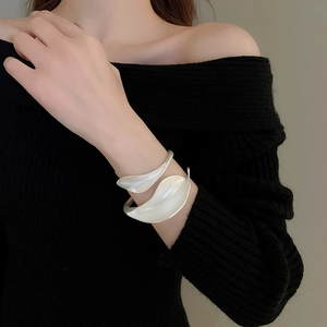 Detail of matte silver leaf-shaped open cuff bracelet worn by model on black knitwear