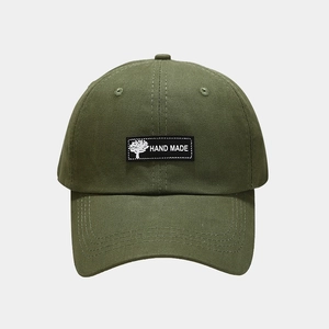 Detail of army green baseball cap featuring a tree icon and Hand Made textile patch