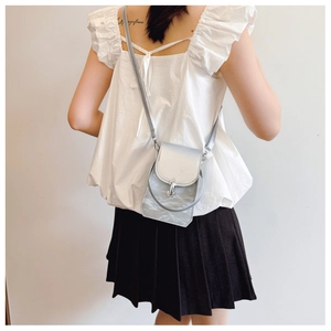 Sac à bandoulière en PU argenté plissé porté par un mannequin en haut blanc et jupe