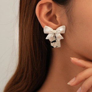 Detail of white resin bow earrings with black and white marble pattern rectangle drop