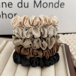 5-piece set of silk satin scrunchies in earthy tones on a beige velvet jewelry tray