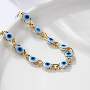 Close-up of golden evil eye bracelet with blue beads on a white minimalist tray