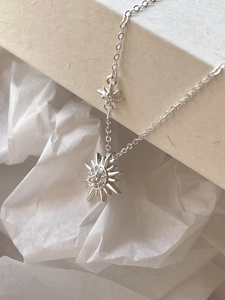 Detailed view of silver sunburst and star pendant necklace with zircon on beige card