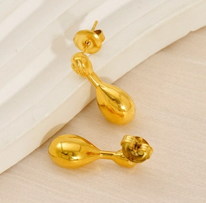 Detail view of golden teardrop stud earrings on warm textured background with butterfly backs