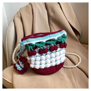 Detail of knit bucket bag featuring 3D cherry accents and elegant pearl shoulder strap