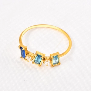 Gros plan d'une bague dorée ornée de trois pierres bleues et de zircons blancs