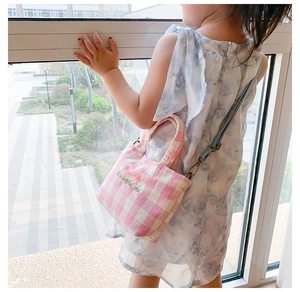 Girl wearing a pink gingham canvas crossbody bag with embroidered lettering in soft natural light