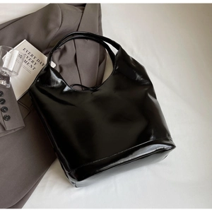 Close-up of a glossy black patent leather tote bag styled with a professional suit and book