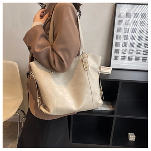 Detail view of large beige PU leather tote bag with gold hardware worn on shoulder