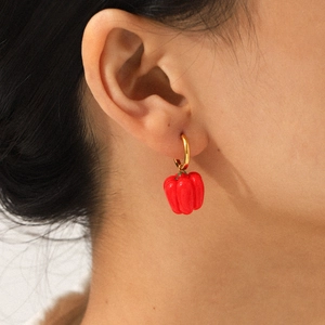 Close-up of a model wearing a gold hoop earring with a vibrant red bell pepper pendant