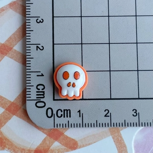 Miniature resin skull figurine with orange eye details next to a ruler for scale