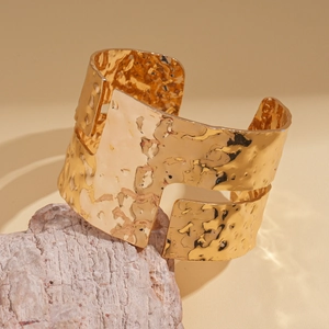 Detailed view of wide gold-plated metal cuff featuring irregular hammered texture and cut-out