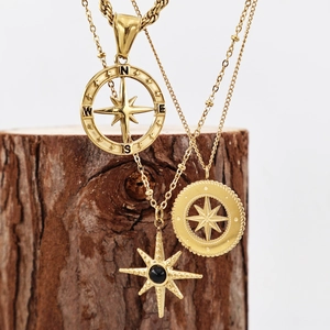 Golden stainless steel compass and north star pendant necklaces on a wooden branch