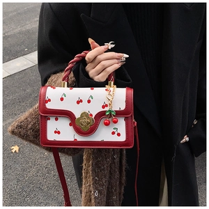Detail of white cherry print handbag featuring woven handle and gold clover clasp