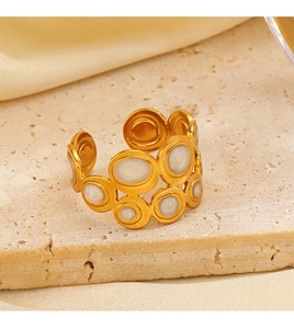 Detail of gold-plated geometric ring featuring a white inlay on a stone surface