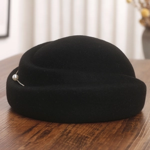 Détail de béret en laine noire avec une grande perle et une fine chaîne métallique
