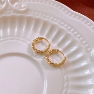 Macro shot of gold twisted hoop earrings with zircon pavé on a white ceramic plate