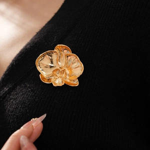 Close-up of a golden orchid flower brooch with detailed texture on a black knit garment