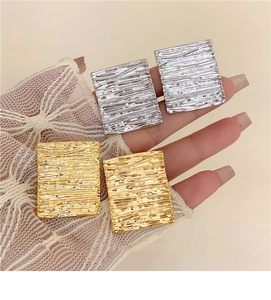 Detail of geometric square textured earrings in gold and silver finish with lace gloves