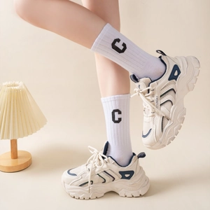 Close-up of chunky cream sneakers with blue panels and embroidered letter C crew socks