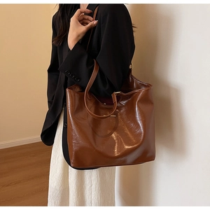 Detail view of a glossy brown PU leather tote bag with slim shoulder straps and metal buckle