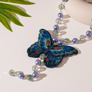 Macro detail of embroidered butterfly pendant with blue-green gradients and crystal beads