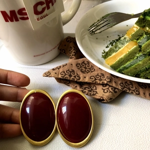 Detail shot of vintage oval burgundy stud earrings with gold trim held over a cafe setting
