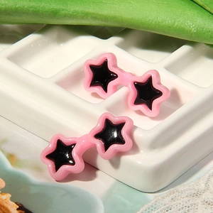 Close-up of pink star-shaped stud earrings for dolls on a white grid display tray