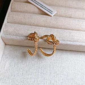 Golden C-shaped twisted knot hoop earrings with textured metal finish in jewelry box