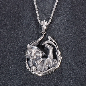 Detail of silver cat pendant with gemstone eyes and leaf accents on a twisted chain