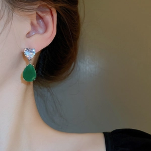 Close-up of heart zircon and green teardrop gemstone earrings worn by a model