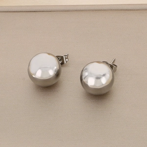Close-up of minimalist silver stainless steel ball stud earrings on a textured background