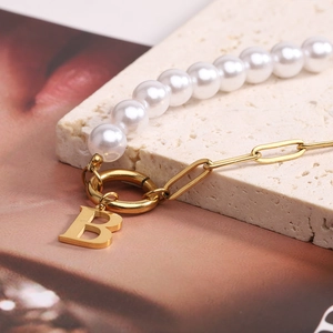 Detailed close-up of golden paperclip chain bracelet with pearls and letter B pendant