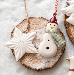 Close-up of white star and snowman ornaments on a wooden slice with faux snow