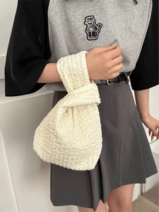 Close-up of beige knot wrist bag with bubble textured fabric carried by a model