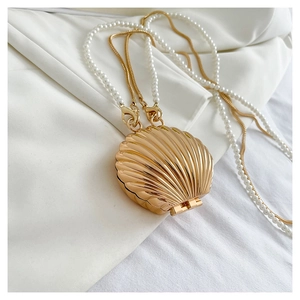 Detail view of a shell-shaped gold metal handbag with pearl chain and textured surface