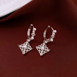Boucles d'oreilles losange en or 18 carats avec perles et cristaux sur fond rouge