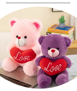 Pink and purple plush teddy bears holding Love hearts sitting on a cozy desk setup