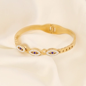 Detail eines goldenen Evil-Eye-Armbands mit blauen Steinen auf weißer Seide