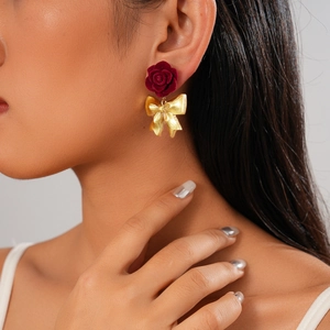 Dettaglio di orecchini a rosa rossa floccata con fiocco dorato indossati da modella
