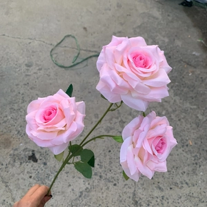 Macro detail of three-headed artificial pink roses with realistic fabric petals and green leaves