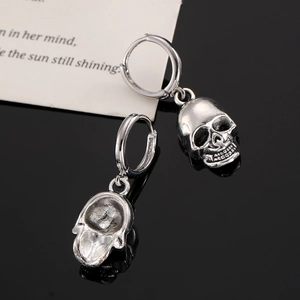 Detailaufnahme von Vintage-Punk-Totenkopf-Ohrringen auf spiegelnder schwarzer Fläche
