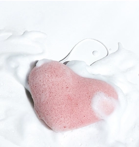 Detail shot of heart-shaped pink konjac sponge with rich cleansing foam on white background