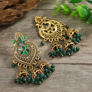 Detail of Jhumka style earrings with green enamel work and beads on a rustic wooden base