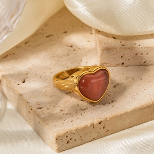 Gros plan d'une bague coeur dorée avec pierre oeil de chat rose sur pierre beige