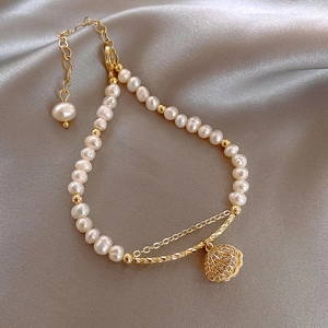 Detail of double-layer gold pearl bracelet featuring a crystal-set shell charm on silk fabric