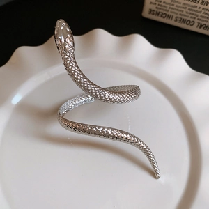 Macro shot of silver snake-shaped jewelry with detailed scales on a white ceramic plate