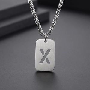 Détail macro du pendentif rectangulaire argenté avec la lettre X sur une finition brossée